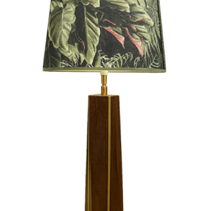 Lampe artisanale en wacapou avec liseré en manil et abat-jour au décor feuillage tropical, présentée sur un buffet dans un salon au style tropical moderne.