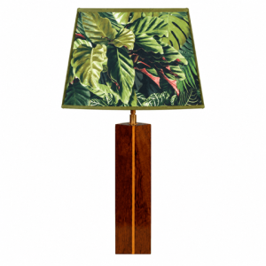 Lampe artisanale en wacapou avec liseré en manil et abat-jour au décor feuillage tropical, présentée sur un buffet dans un salon au style tropical moderne.